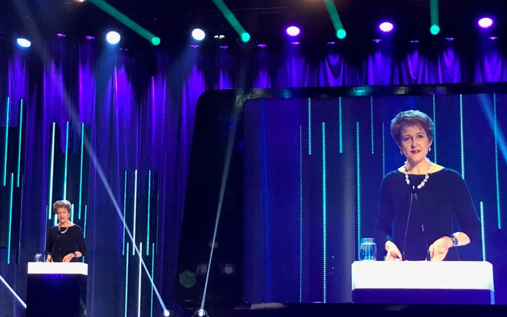 La conseillère fédérale Simonetta Sommaruga parle devant un pupitre, sous les projecteurs. À l’arrière-plan, son image est diffusée sur grand écran.